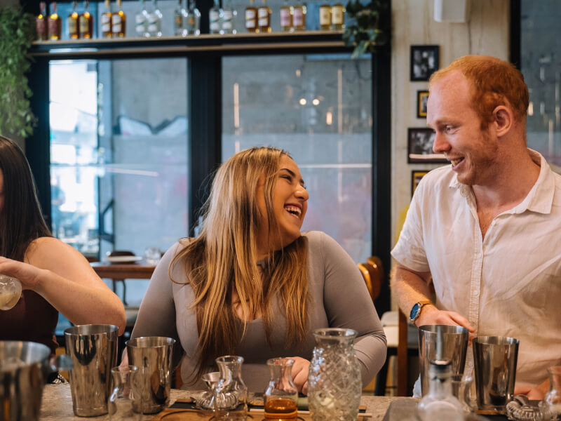 Smiling couple sitting in a bar with cocktail-making equipment around them